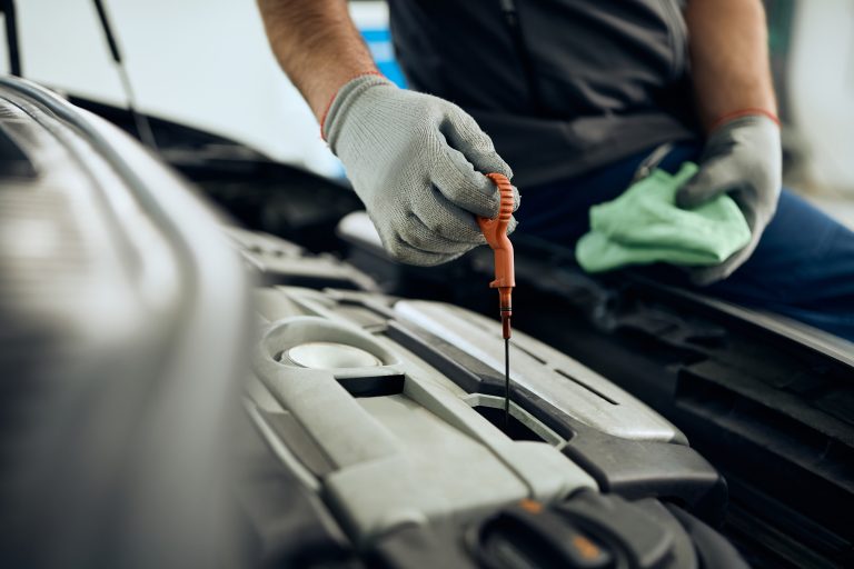Close-up of auto repairman checking oil level during engine maintenance in a workshop