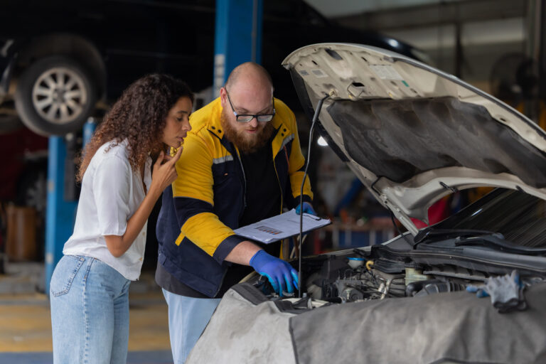 Mechanic checks car engine while customer looks on inside auto r